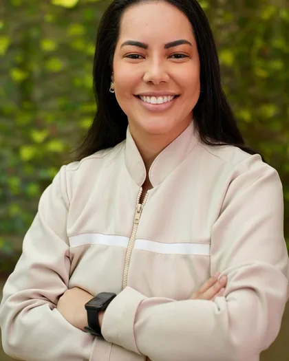 Dra. Laura Ramos Vieira de braços cruzados diante de uma parede de folhagem.